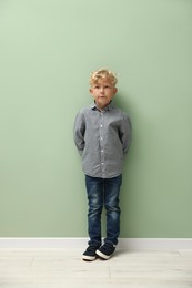 Photo of Cute little boy standing near green wall