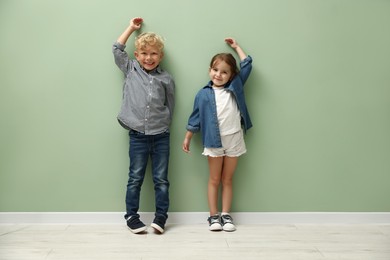 Photo of Cute little girl and boy measuring their heights near green wall