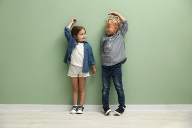 Photo of Cute little girl and boy measuring their heights near green wall