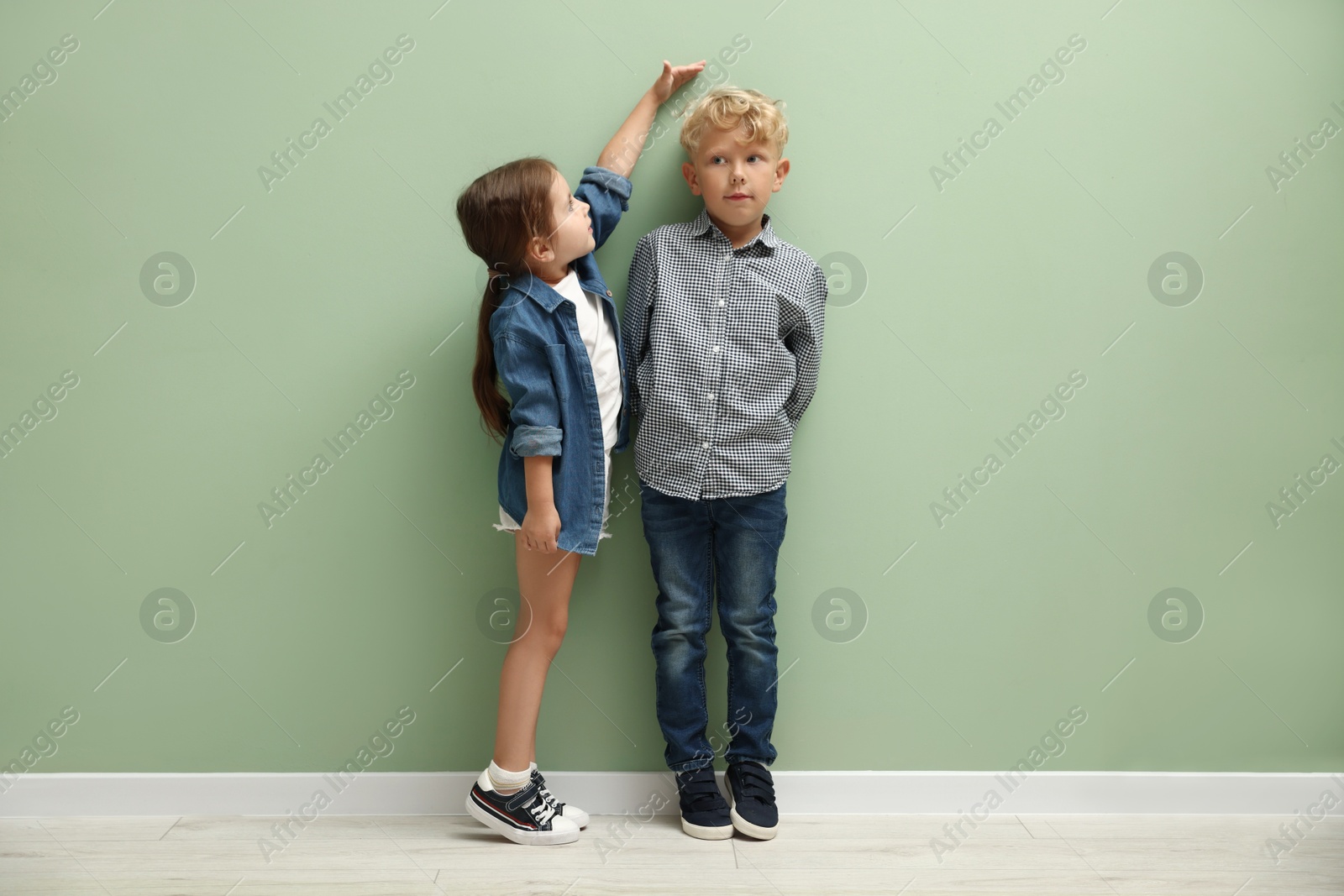 Photo of Cute little girl and boy measuring their heights near green wall
