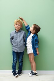 Photo of Cute little girl and boy measuring their heights near green wall