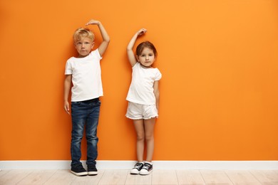 Photo of Cute little girl and boy measuring their heights near orange wall