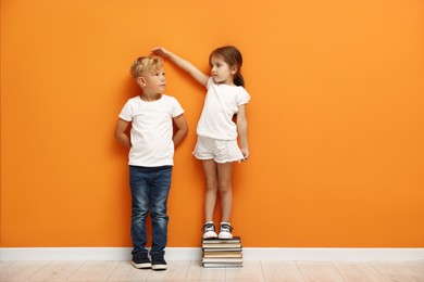 Photo of Cute little girl and boy measuring their heights near orange wall