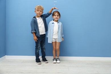 Photo of Cute little girl and boy measuring their heights near blue wall