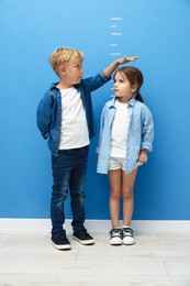 Photo of Cute little girl and boy measuring their heights near blue wall