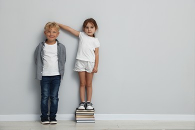 Photo of Cute little girl and boy measuring their heights near light wall. Space for text