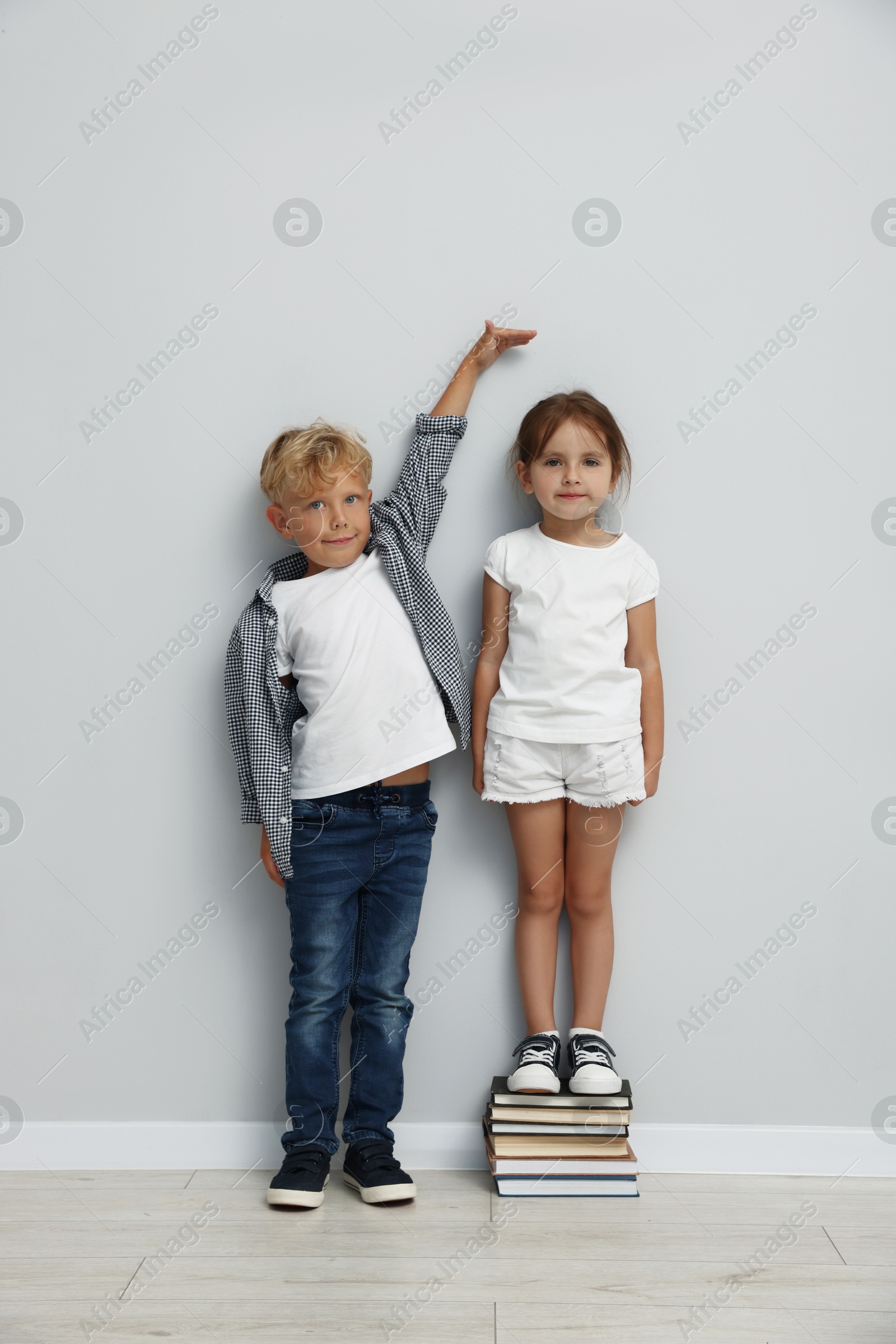 Photo of Cute little girl and boy measuring their heights near light wall