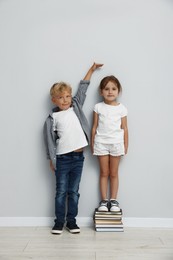 Photo of Cute little girl and boy measuring their heights near light wall