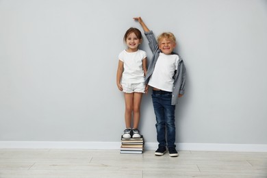 Photo of Cute little girl and boy measuring their heights near light wall