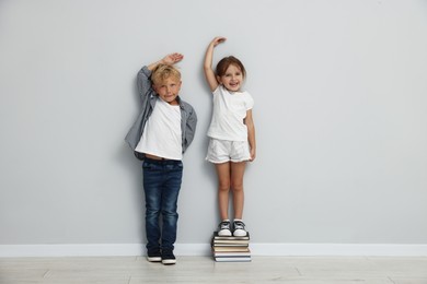 Photo of Cute little girl and boy measuring their heights near light wall