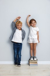 Photo of Cute little girl and boy measuring their heights near light wall