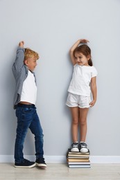 Photo of Cute little girl and boy measuring their heights near light wall