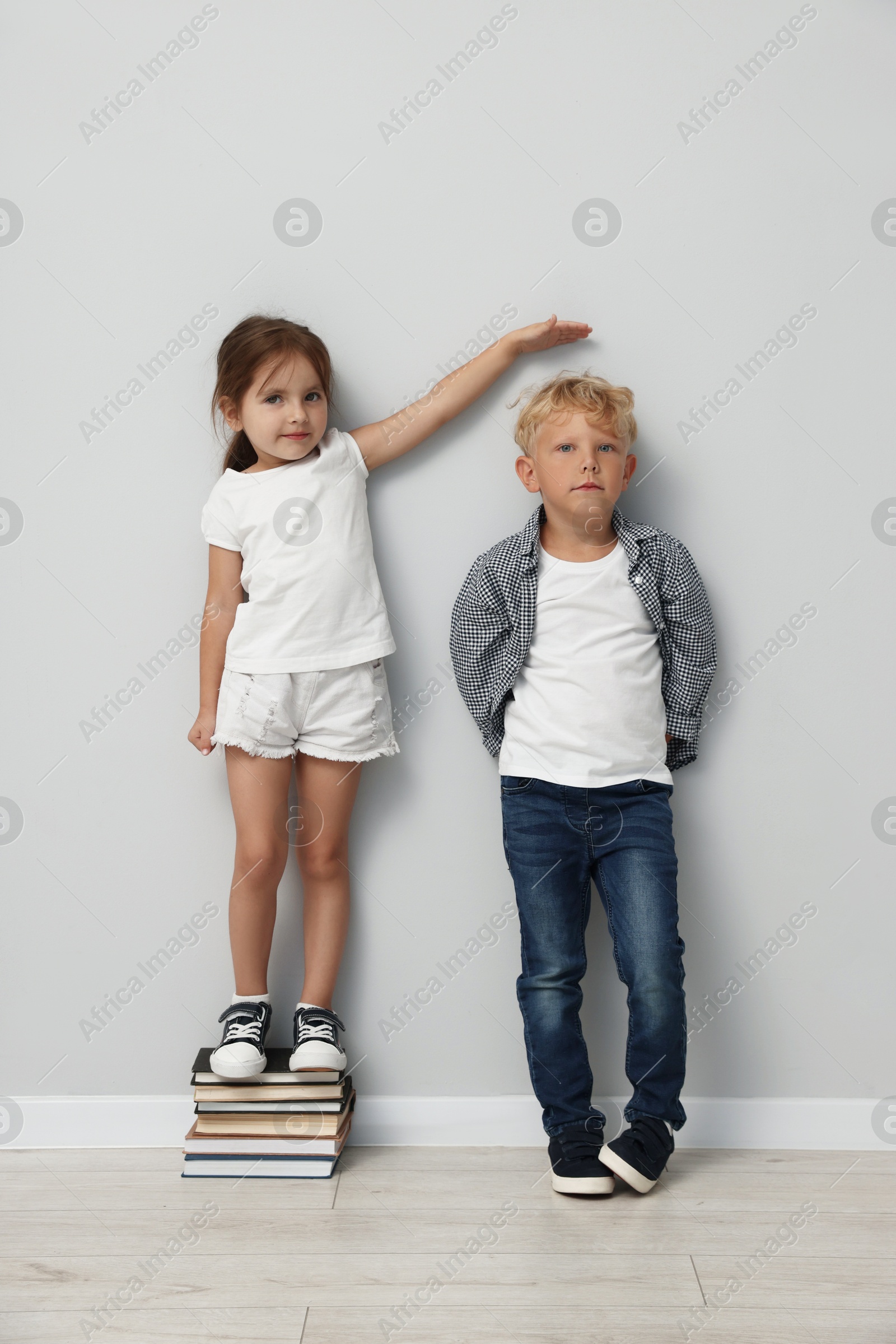 Photo of Cute little girl and boy measuring their heights near light wall