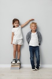 Photo of Cute little girl and boy measuring their heights near light wall