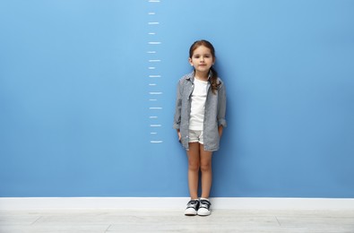 Photo of Cute little girl measuring her height near blue wall