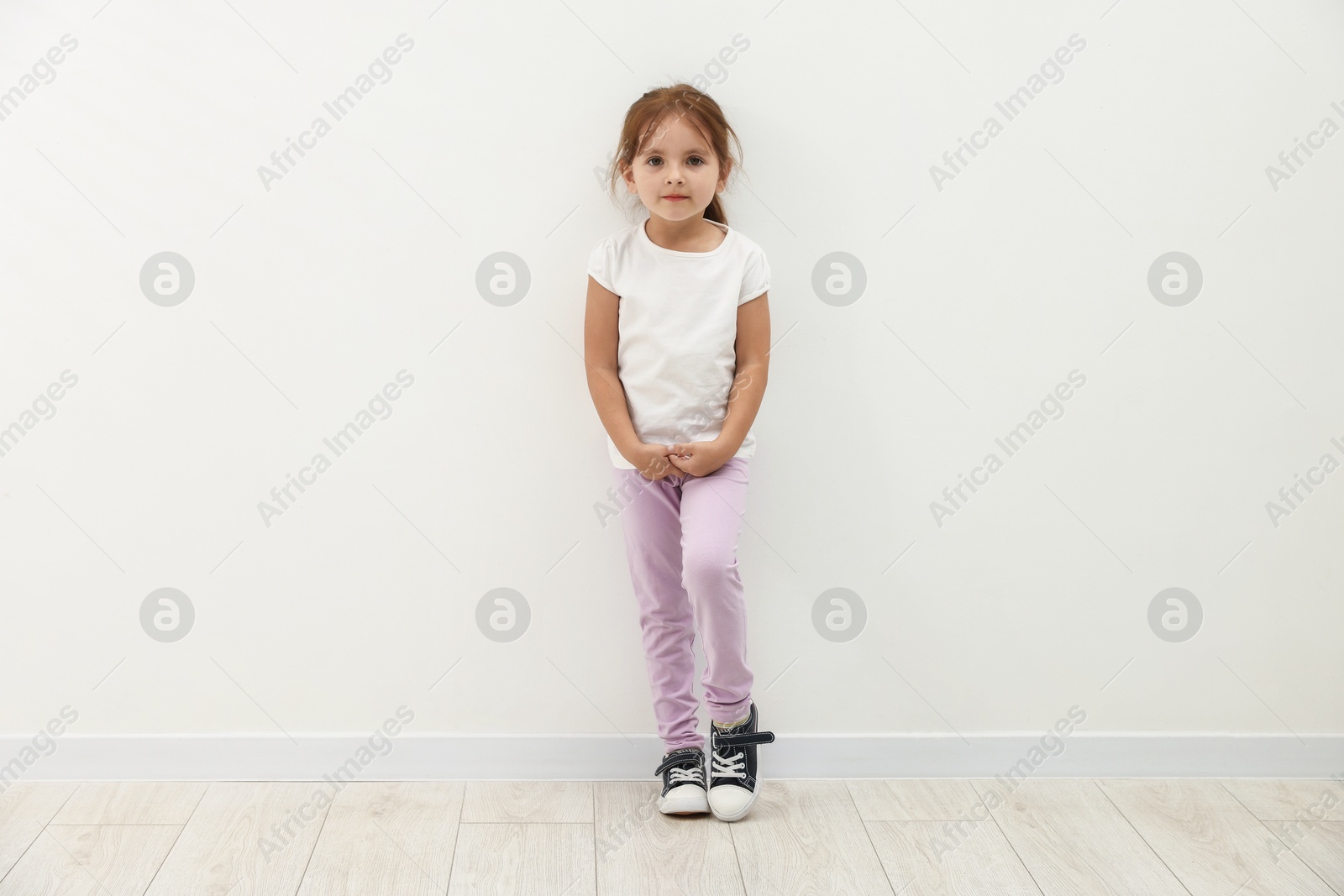 Photo of Cute little girl standing near white wall