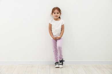 Photo of Cute little girl standing near white wall