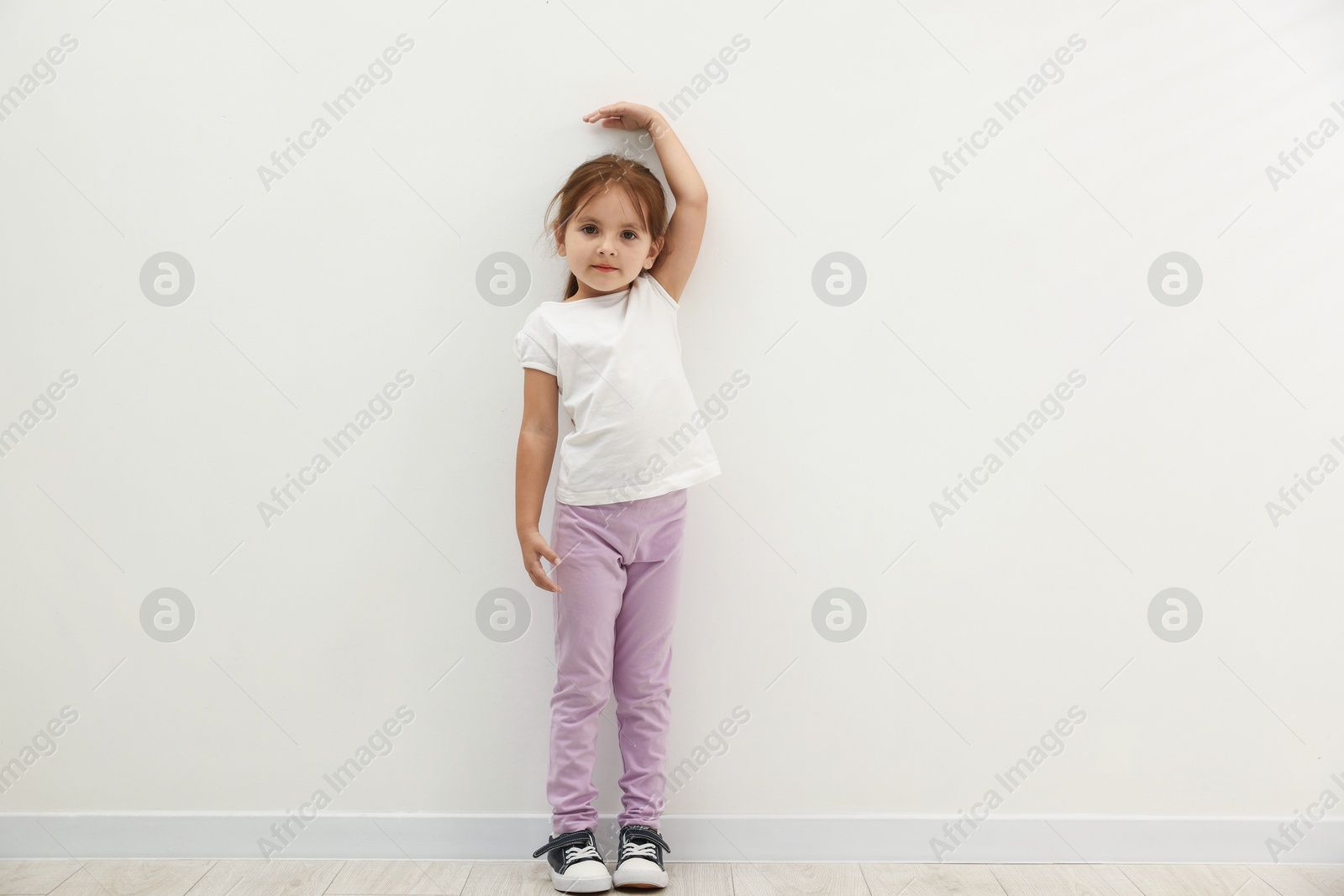Photo of Cute little girl measuring her height near white wall