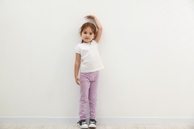 Photo of Cute little girl measuring her height near white wall