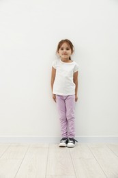Photo of Cute little girl standing near white wall