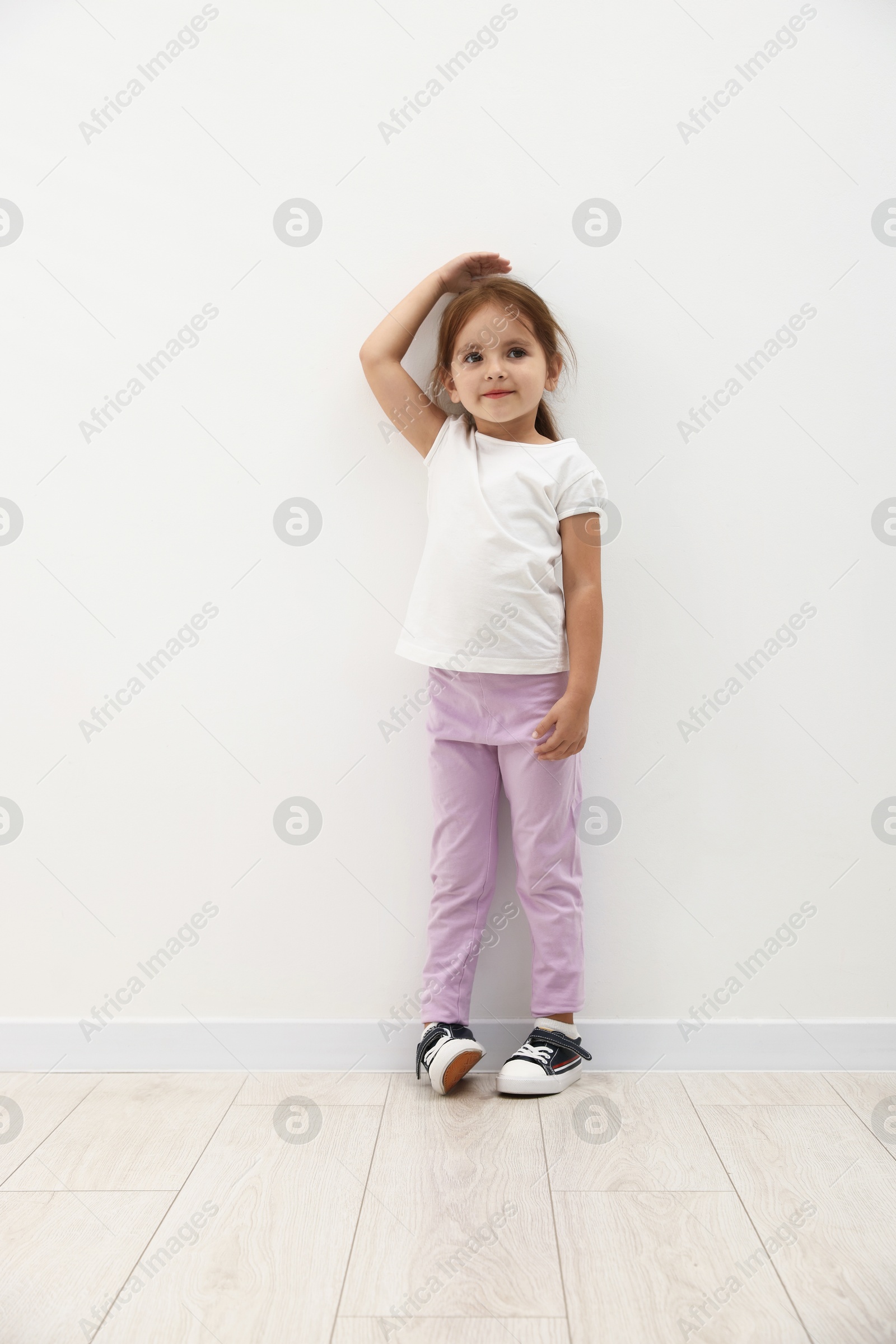 Photo of Cute little girl measuring her height near white wall