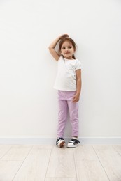 Photo of Cute little girl measuring her height near white wall