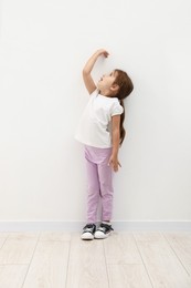 Photo of Cute little girl measuring her height near white wall