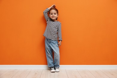 Photo of Cute little girl measuring her height near orange wall