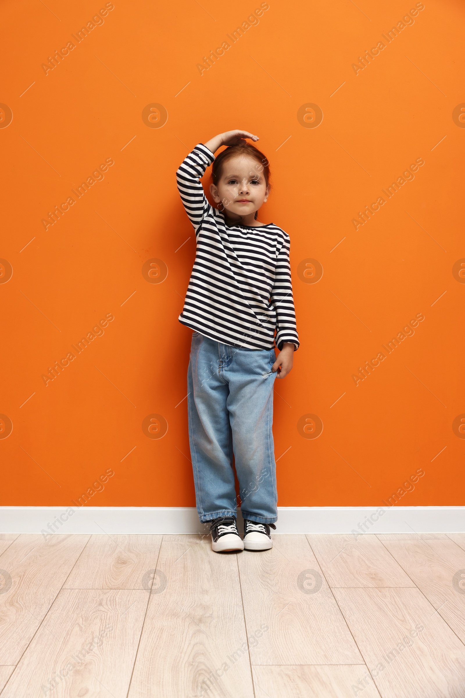 Photo of Cute little girl measuring her height near orange wall