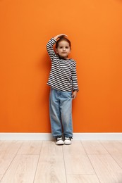 Photo of Cute little girl measuring her height near orange wall