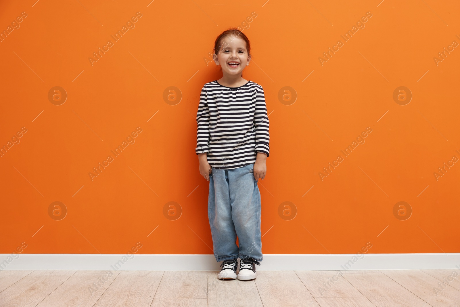 Photo of Cute little girl standing near orange wall