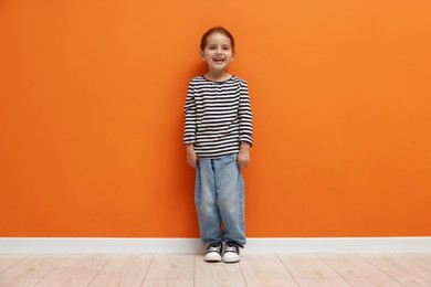 Photo of Cute little girl standing near orange wall