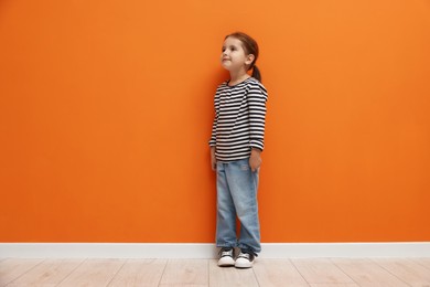 Photo of Cute little girl standing near orange wall