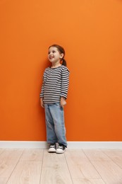 Photo of Cute little girl standing near orange wall