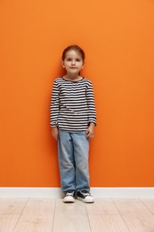 Photo of Cute little girl standing near orange wall