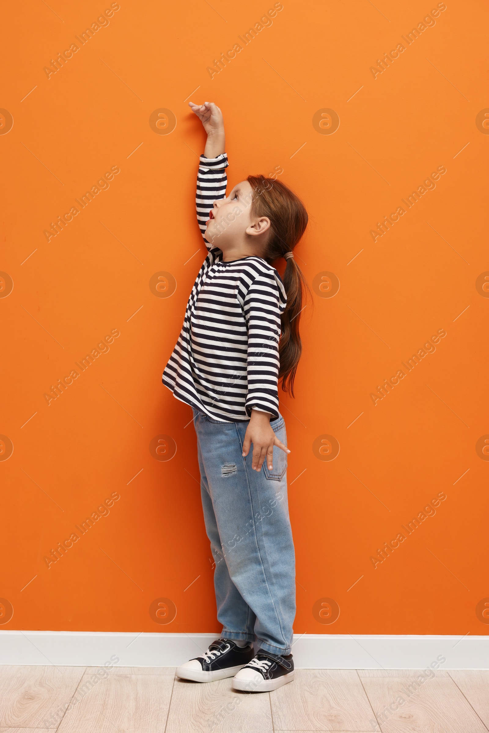 Photo of Cute little girl measuring her height near orange wall