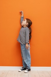Photo of Cute little girl measuring her height near orange wall