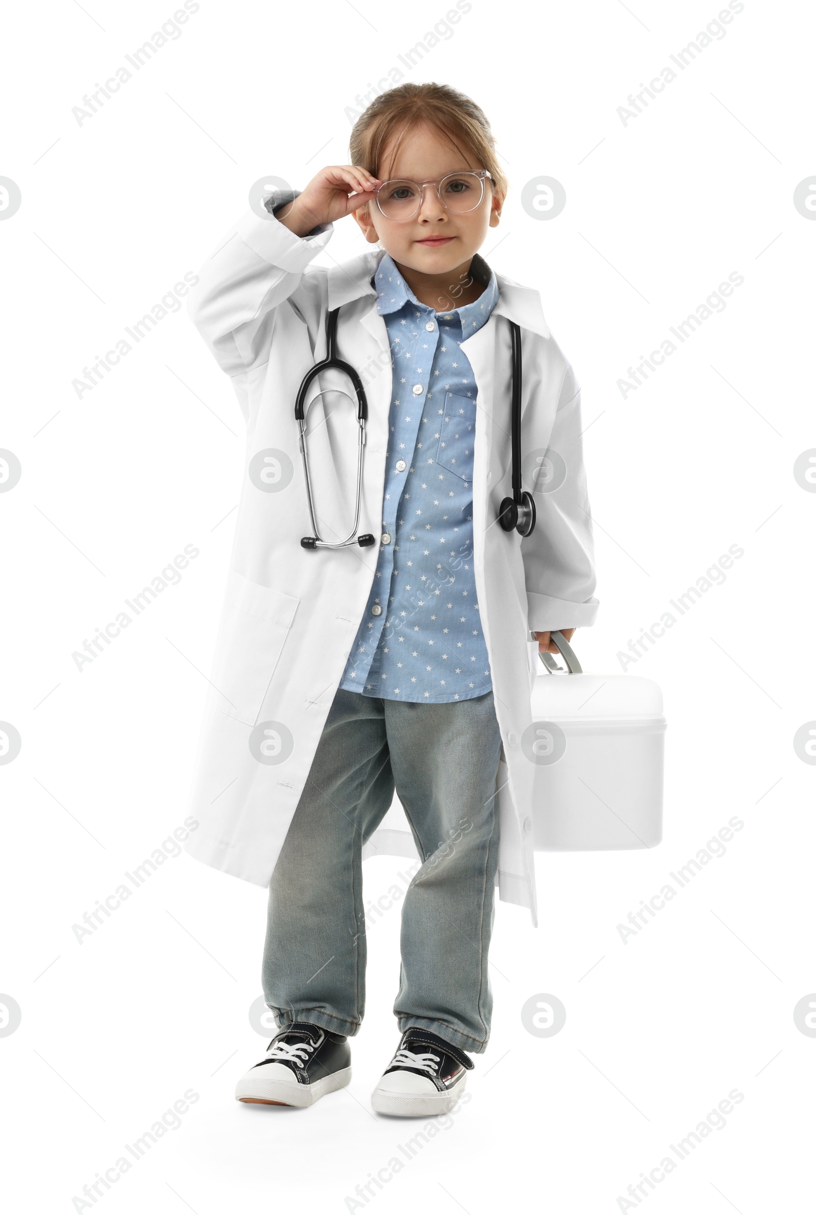 Photo of Choice of profession. Little girl in uniform with stethoscope and case pretending to be doctor on white background