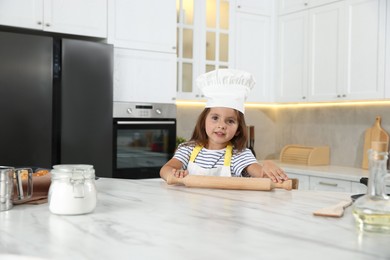 Photo of Choice of profession. Little girl with rolling pin pretending to be chef in kitchen