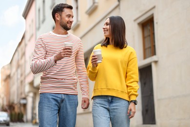 Photo of Coffee to go. Couple with paper cups of drinks walking on city street, low angle view