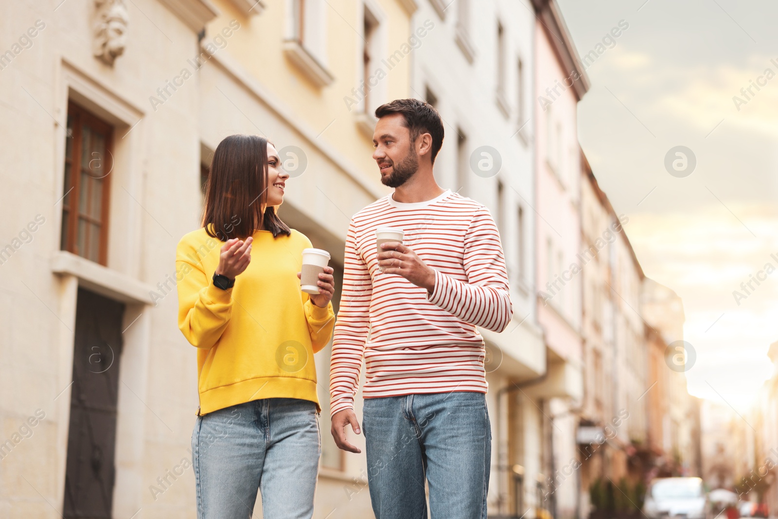 Photo of Coffee to go. Couple with paper cups of drinks walking on city street, low angle view. Space for text