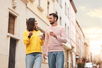 Photo of Coffee to go. Couple with paper cups of drinks walking on city street, low angle view. Space for text