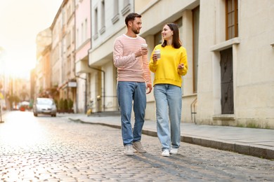 Photo of Coffee to go. Couple with paper cups of drinks walking on city street, space for text