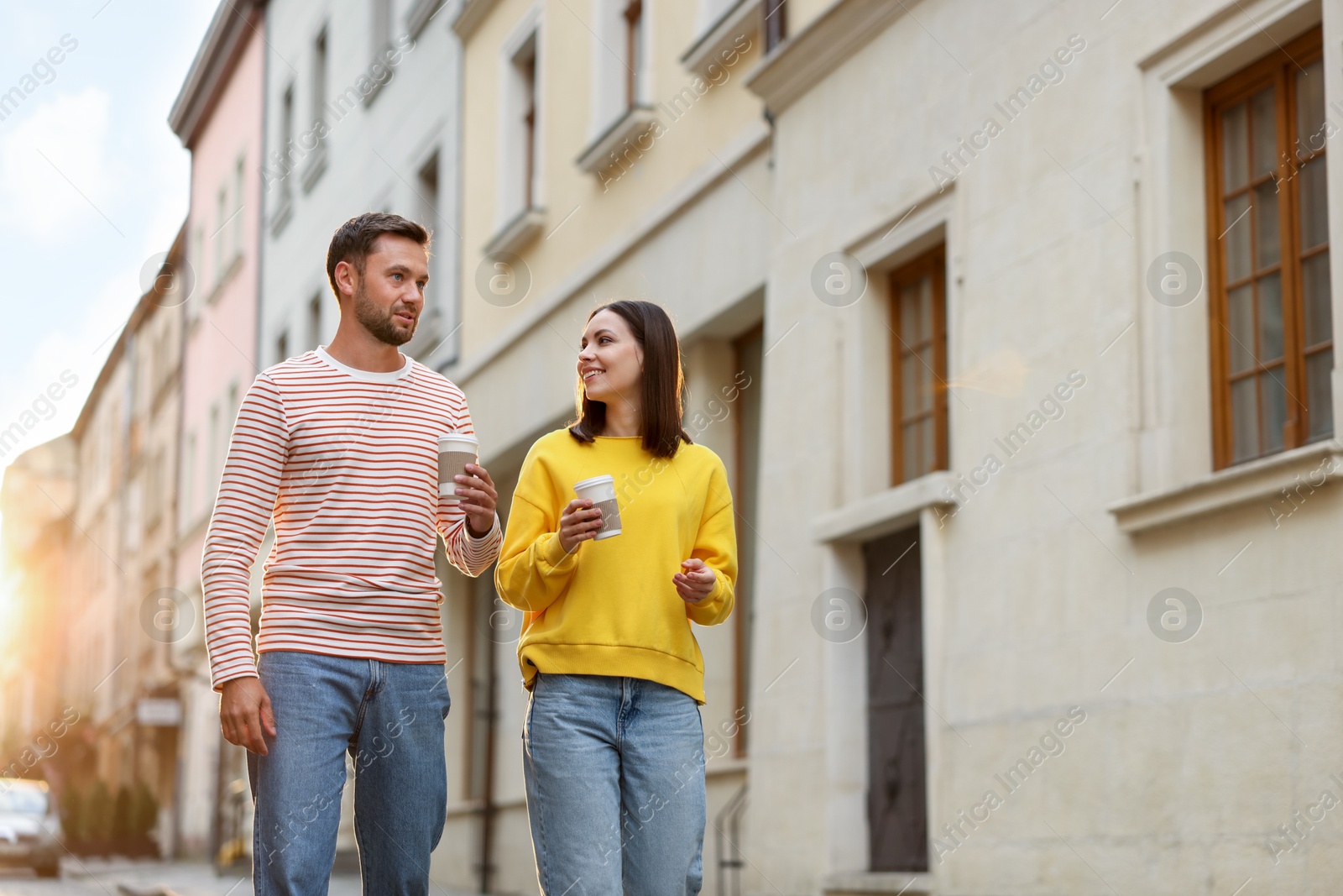 Photo of Coffee to go. Couple with paper cups of drinks walking on city street, low angle view. Space for text
