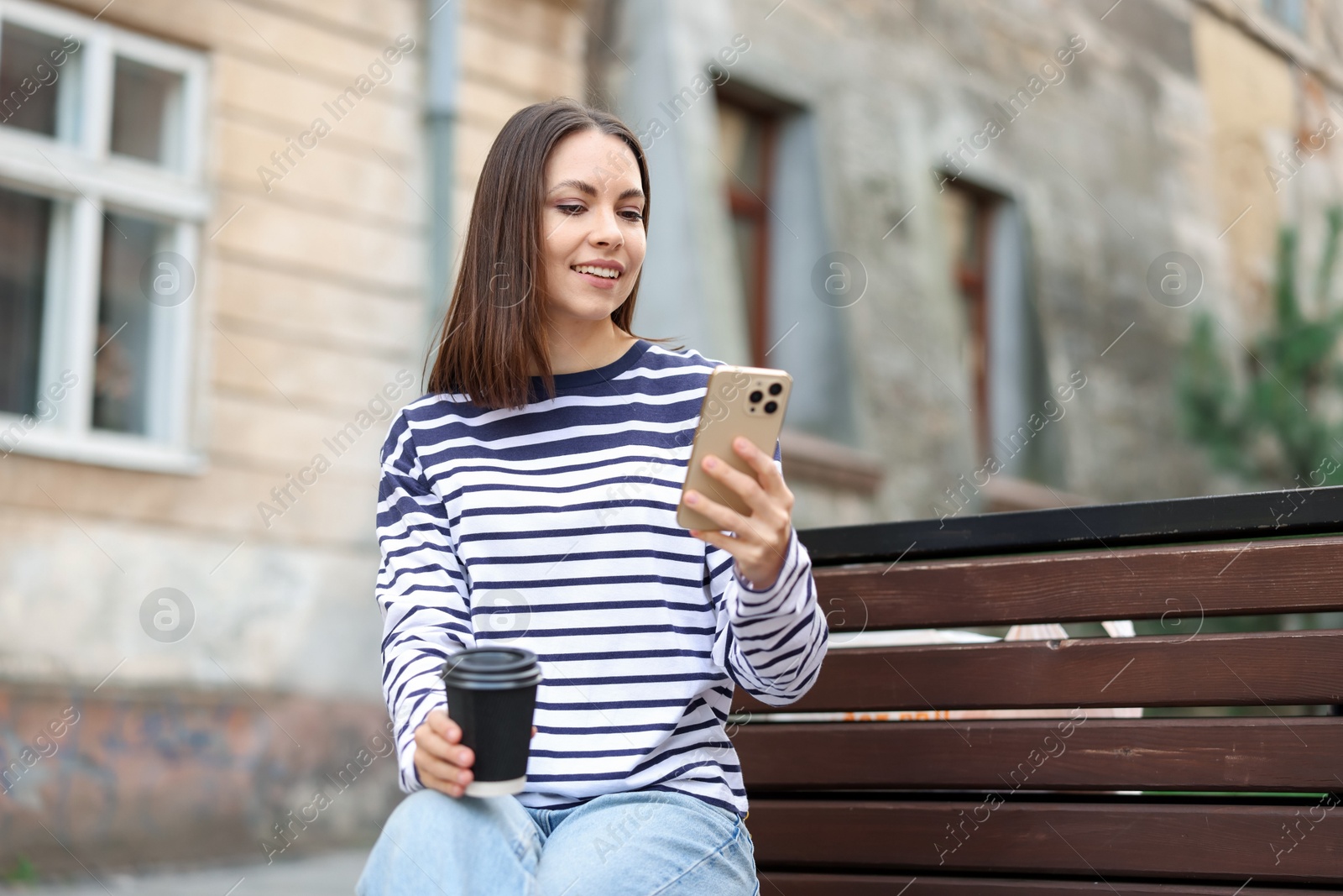 Photo of Coffee to go. Woman with paper cup of drink and smartphone on bench outdoors