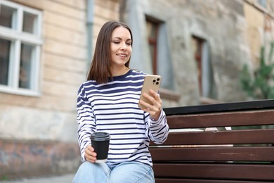 Photo of Coffee to go. Woman with paper cup of drink and smartphone on bench outdoors