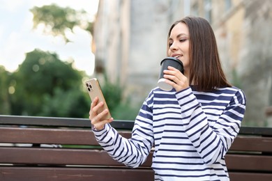 Photo of Coffee to go. Woman with paper cup of drink and smartphone on bench outdoors