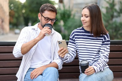 Photo of Coffee to go. Couple with paper cups of drinks and smartphone on bench outdoors
