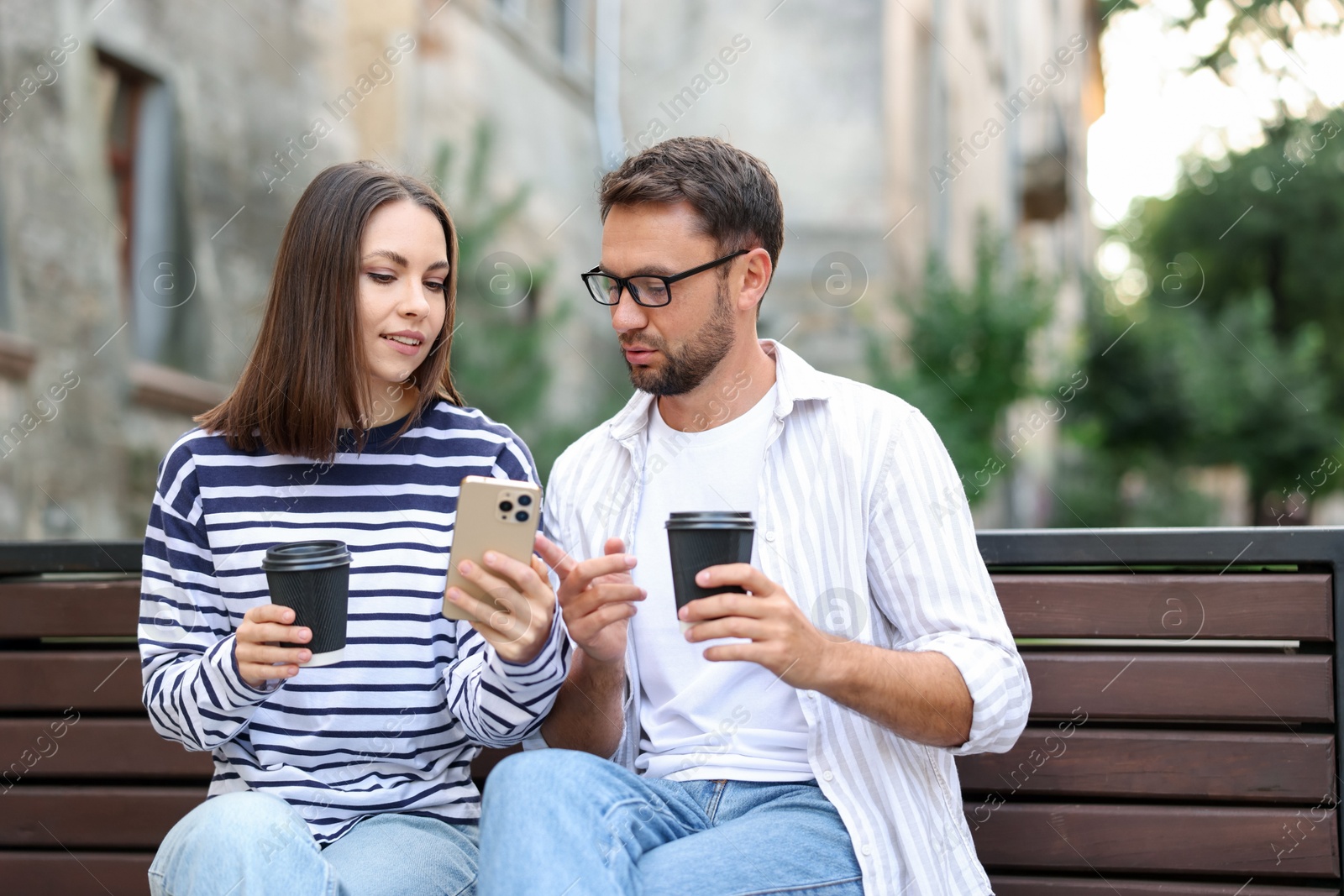 Photo of Coffee to go. Couple with paper cups of drinks and smartphone on bench outdoors
