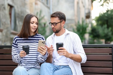 Photo of Coffee to go. Couple with paper cups of drinks and smartphone on bench outdoors